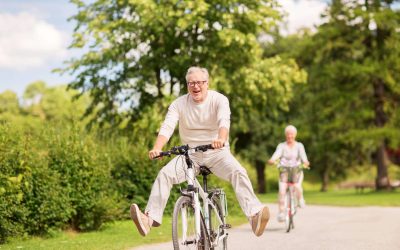 Joyful elderly man riding a bike with legs extended, enjoying a sunny day.